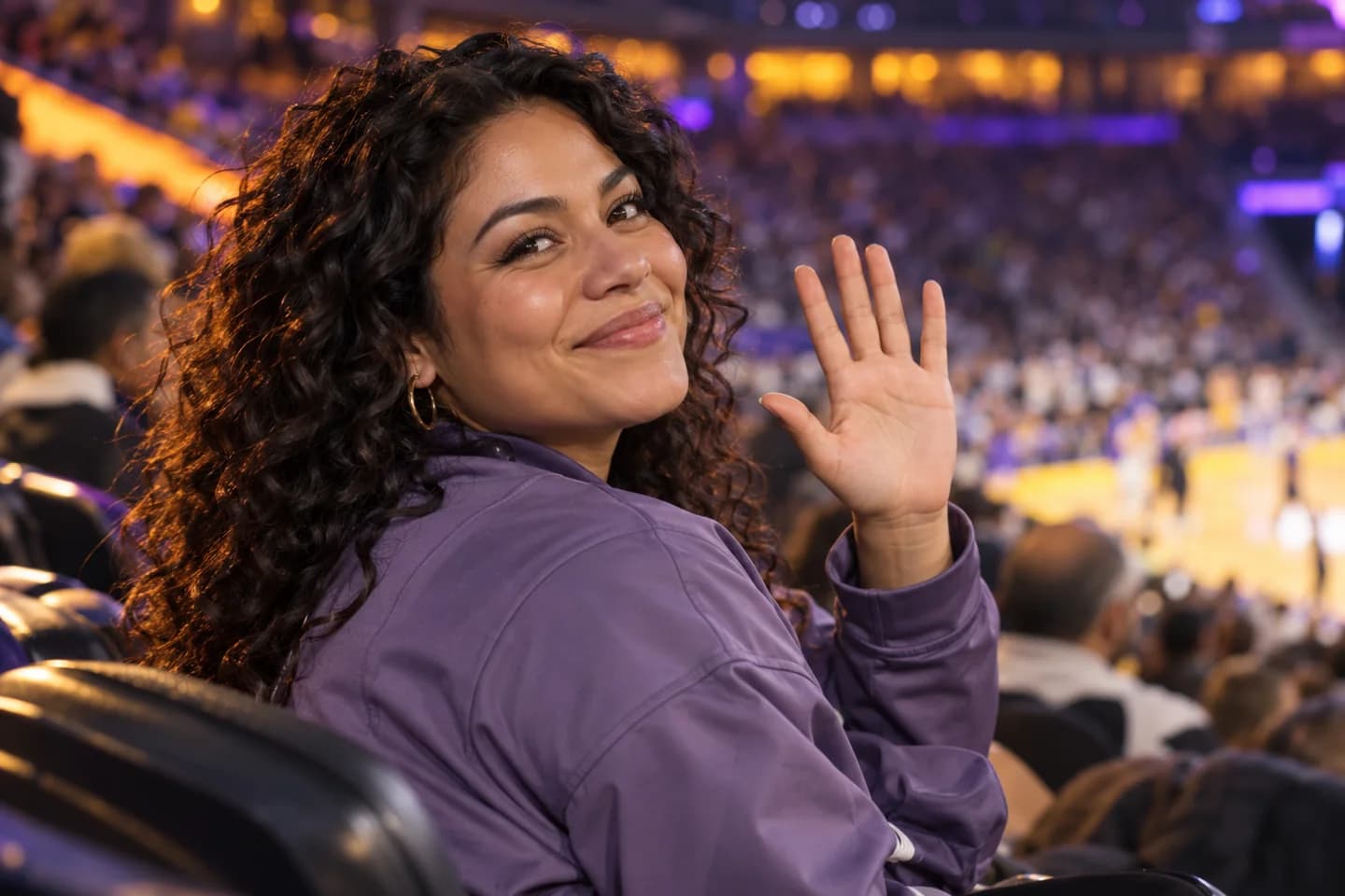 Curly-haired basketball spectator greeting the crowd camera beneath amber and violet arena lights