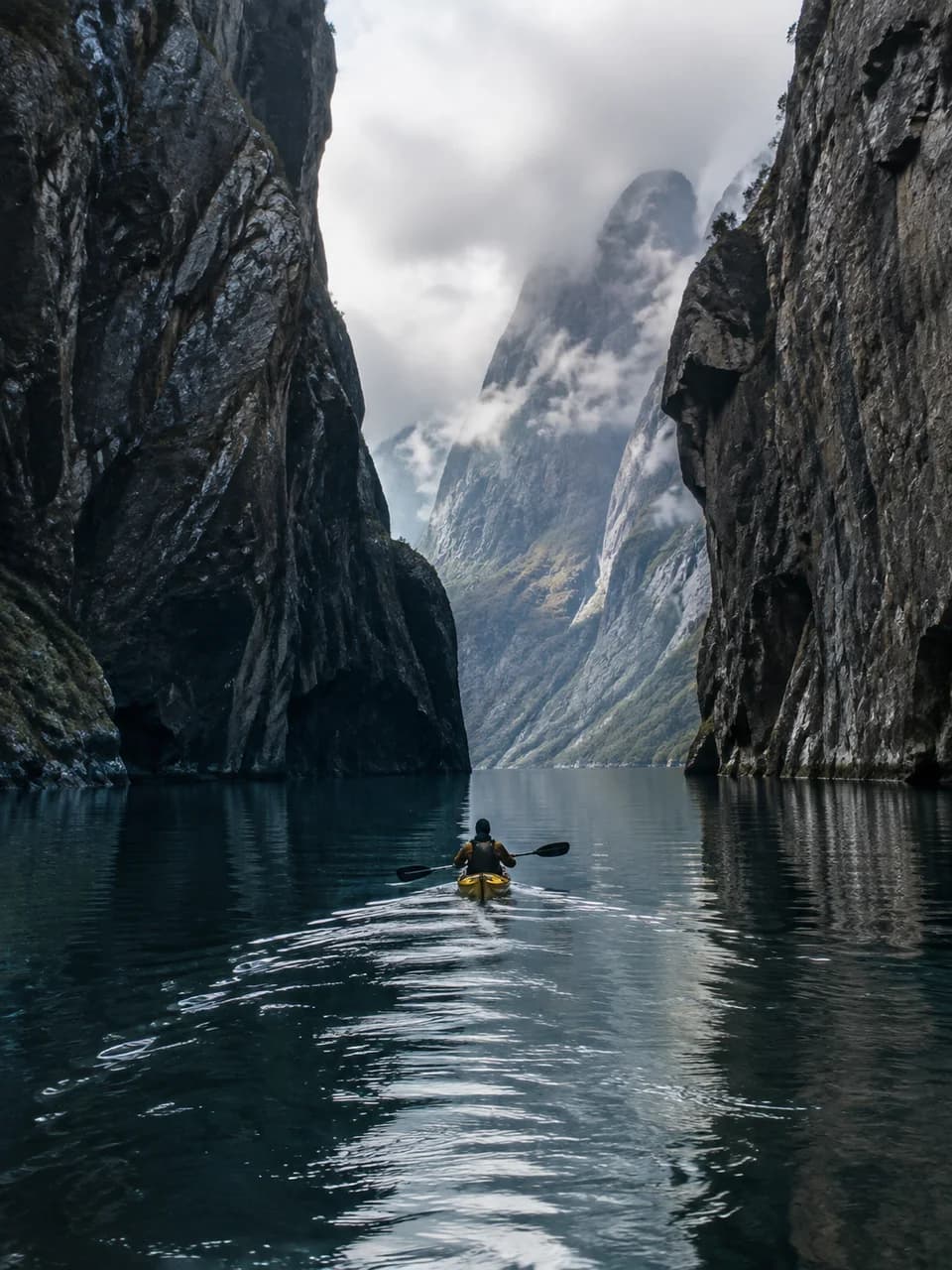Yellow kayak moving between tall Nordic fjord cliffs